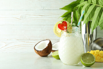Glass of tropical cocktail and ingredients on white textured table