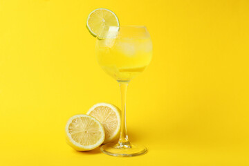 Glass of lemon cocktail and ingredients on yellow background