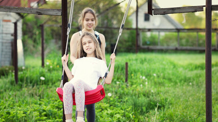 Cheerful children in light clothes ride a street swing in a blooming green home garden and laugh in a happy smile