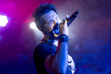 Young energetic singer performing in a club under colorful led lights - Powered by Adobe