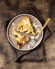 Two pieces of homemade shortbread pie with milk and bitter chocolate and almonds in a plate on a brown table close-up. Delicious sweet pastries	