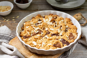 Homemade shortbread pie with milk and bitter chocolate in a baking dish on a gray wooden culinary background close-up. Delicious rustic sweet pastries