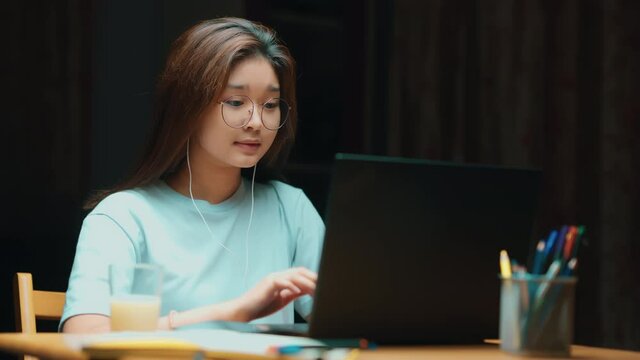 Happy Asian teenage girl student online learning class study online video call with the teacher at night, with laptop at home. New normal.Covid-19 coronavirus.Social distancing. stay home.