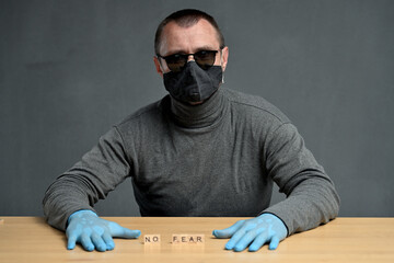 Concept Adult man in a mask and glasses sits at a table with the text no fear on the cubes