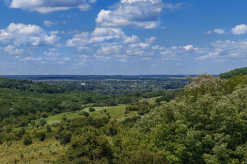 Rural landscape with green fields and sparsely wooded areas. Beautiful summer landscape with fields and green vegetation under a blue sky with white cumulus clouds in the countryside.