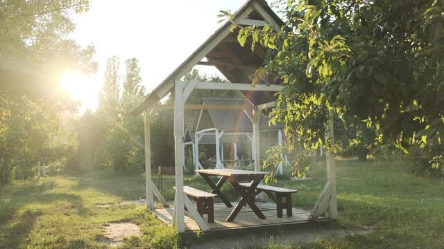 Empty gazebo for rest and picnic next to the barbecue in the park during sunset. Wooden summer house for vacationers in the forest