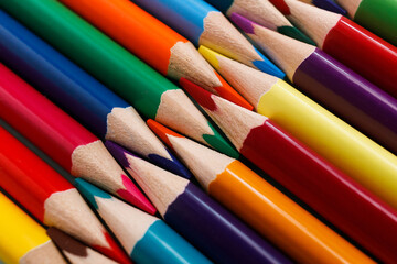 Naklejka premium Colored sharpened pencils lie in a row close-up. Solid abstract background of wooden multi-colored pencils. These are school supplies.