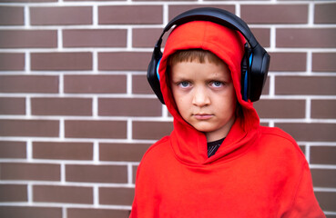 Photo of concentrated boy child listening music with headphones. Serious looking teenager with earphones on background of red bricks. High quality photo