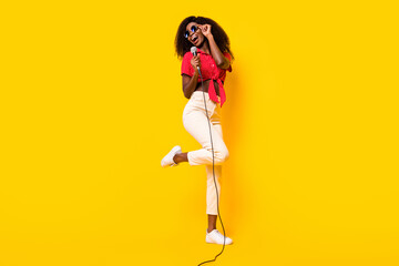 Full length photo of happy afro american woman look empty space sing mic isolated on yellow color background