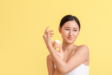 Beautiful young woman with facial cream on color background