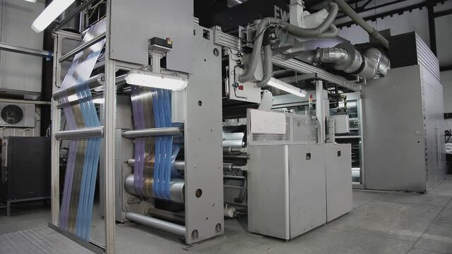 A large machine for printing on packaging works at the factory. The factory produces packaging. The machine applies a drawing on the packaging made of paper, glass, plastic and other things.