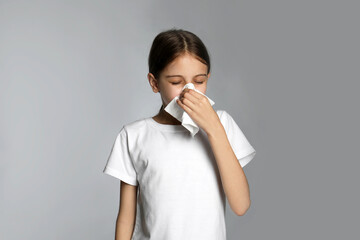 Little girl blowing nose into paper tissue on light grey background. Seasonal allergy
