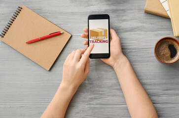 Woman holding mobile phone with open page of delivery service application on color wooden table