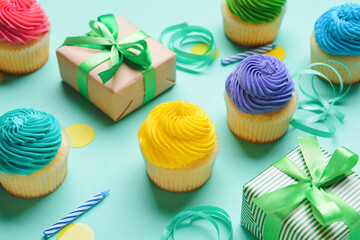 Tasty Birthday cupcakes, gifts, candles and ribbons on color background, closeup