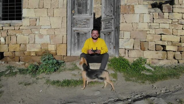 Aerial view of dead village on the top of mountain. Ancient buildings, stone ruins of ancient city. Man is sitting outside the house and stroking dog. Impressive mountainous natural landscape