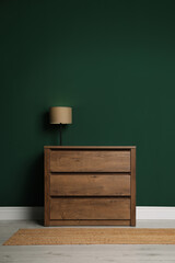 Modern wooden chest of drawers with lamp near green wall indoors