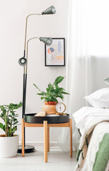 Stylish alarm clock and houseplant on table in bedroom