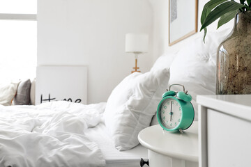 Stylish alarm clock on table in bedroom