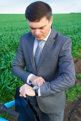 Businessman with a bicycle looking at his wristwatch in a green grass field - business concept for freedom, vacation or freelance. Beautiful spring nature.