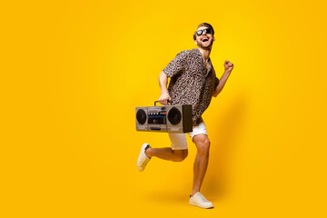 Full length photo of lucky sweet gentleman dressed print shirt glasses running holding boombox isolated yellow color background