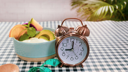 Fototapeta na wymiar Close up of Alarm clock with delicious natural yogurt fruit parfait mint and fresh fruit in the kitchen garden -Diet slim of intermittent fast concept