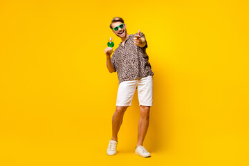 Fototapeta na wymiar Full length photo of attractive cute gentleman dressed print shirt glasses drinking cocktail pointing you isolated yellow color background