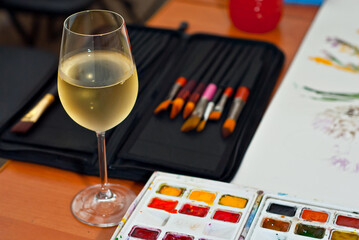 Glass of white wine close up. Wine on a palette background with paints. The concept of creativity and inspiration.