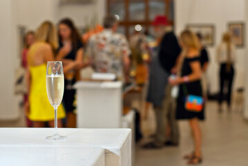 Glasses with wine on the background of the exhibition of paintings. People blurred in the background. Art salon with white walls. - obrazy, fototapety, plakaty