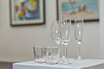 Empty wine glasses on the background of the exhibition of paintings. Artwork blurred in the background. Art salon with white walls.