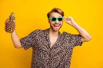 Photo of sweet charming young gentleman dressed print shirt arm dark glasses holding pineapple isolated yellow color background