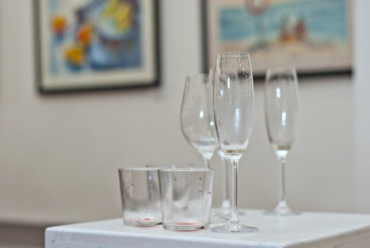 Empty wine glasses on the background of the exhibition of paintings. Artwork blurred in the background. Art salon with white walls.