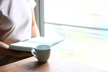 white ceramic cup on table with woman student review lessons at home during online learning