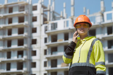 An engineer discusses the construction process on the phone against the background of a multi-storey building under construction