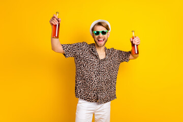 Photo of charismatic cute young gentleman dressed print shirt glasses headwear holding beer bottles isolated yellow color background