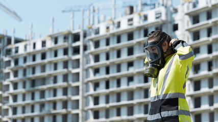 An employee of the gas and environmental inspection puts on a gas mask against the background of an industrial unfinished building