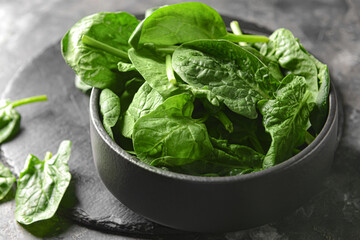 Bowl with fresh spinach leaves on grey background, closeup