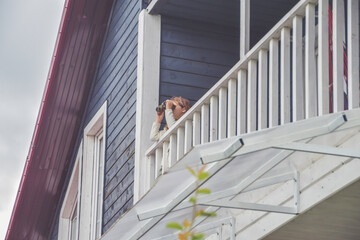 the child girl looks through binoculars standing on the balcony of the house