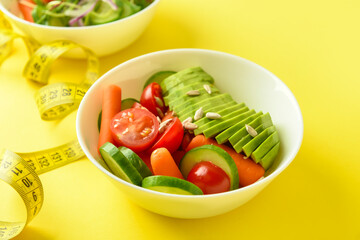 Bowl with delicious vegetable salad and measuring tape on color background
