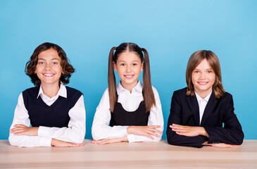 Photo of charming sweet schoolkids formalwear smiling sitting table arms folded listening lesson isolated blue color background