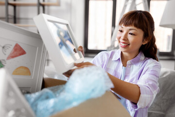 moving, people and real estate concept - happy smiling asian woman unpacking boxes at new home