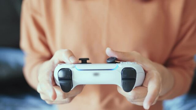 Closeup - Hands holding controller presses buttons on game joystick and play TV game.