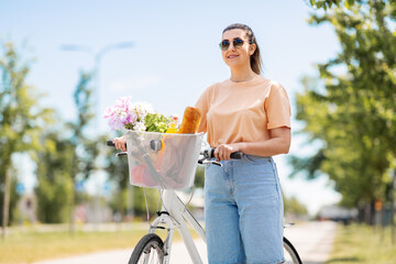 people, leisure and lifestyle - happy young woman with food and flowers in basket of bicycle on city street