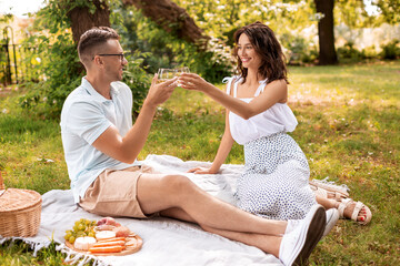 leisure and people concept - happy couple with drinks and food having picnic at summer park