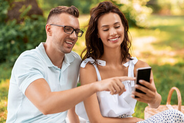 leisure and people concept - happy couple with smartphone having picnic at summer park