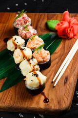 japanese sushi rolls with cheese cap and roll with raw salmon and tuna in a restaurant serving on a wooden board on a dark background. top view.