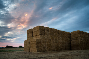 Piled hay bales on a field against sunrise sky