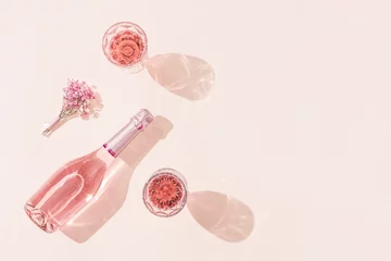 Gordijnen Bottle of rose wine, two glasses with drink, small bouquet of flowers in bright sunlight. Summer romance concept. © yrabota