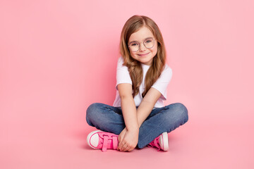 Obraz na płótnie Canvas Photo of cute lovely small girl sit floor hands hold wear specs white t-shirt jeans shoes isolated pink color background