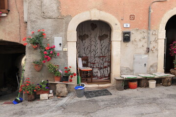 Rural Village Street View with House Facade, Arched Door, Wooden Bench and Flowers in Central Italy