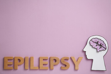 Word Epilepsy made of wooden letters near human head cutout with brain on pink background, flat...